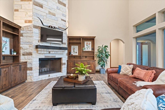 living area with arched walkways, a high ceiling, a stone fireplace, and wood finished floors