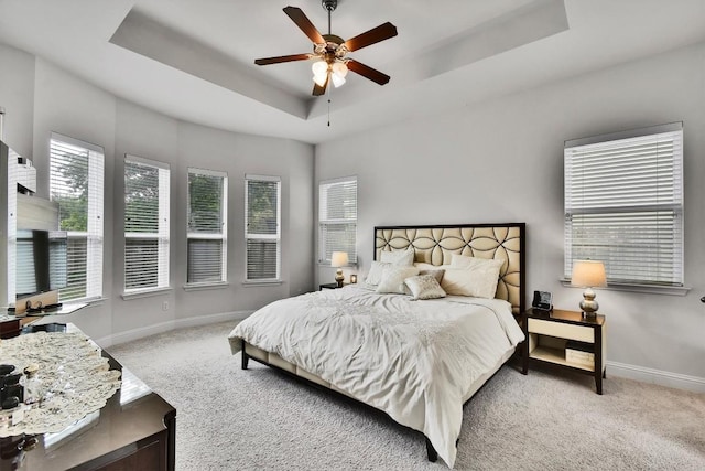 carpeted bedroom featuring a ceiling fan, a tray ceiling, and baseboards