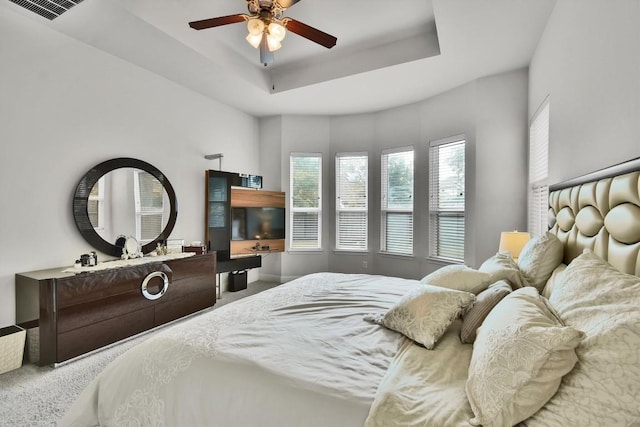 carpeted bedroom featuring a ceiling fan, a tray ceiling, and visible vents
