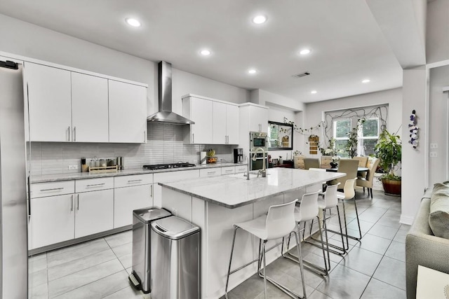 kitchen with a kitchen breakfast bar, visible vents, a sink, stainless steel appliances, and wall chimney exhaust hood