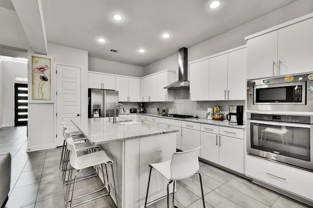 kitchen with appliances with stainless steel finishes, a sink, light tile patterned floors, a breakfast bar, and wall chimney exhaust hood