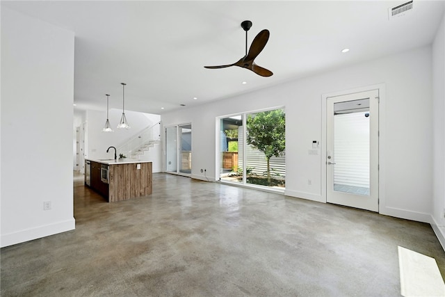unfurnished living room with ceiling fan, visible vents, a sink, baseboards, and stairs