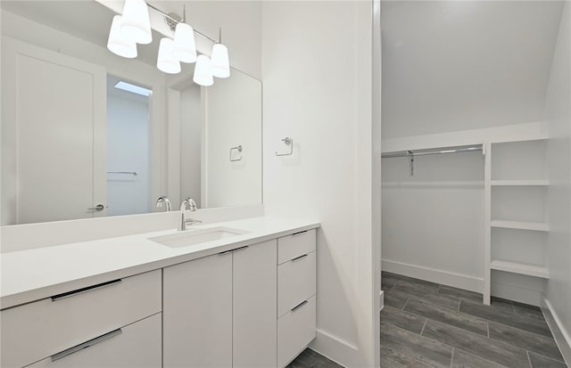 bathroom featuring baseboards, vanity, wood finished floors, and a walk in closet