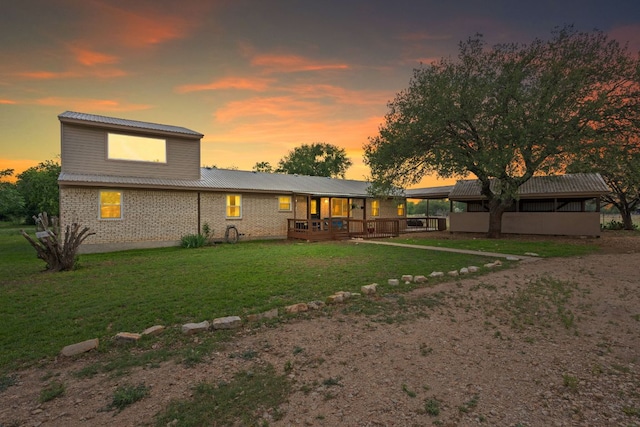 back of house at dusk featuring a lawn, brick siding, metal roof, and a sunroom