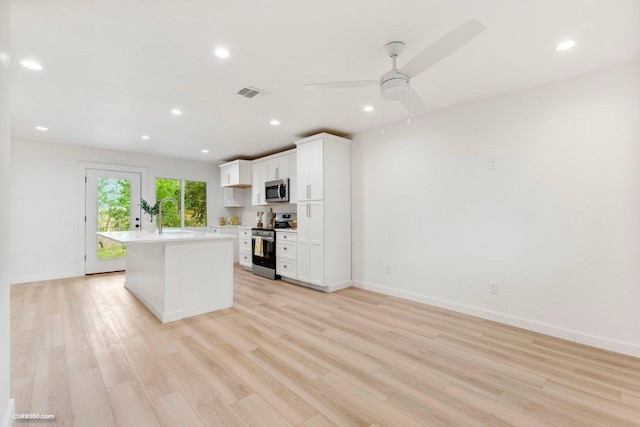 kitchen featuring light countertops, an island with sink, stainless steel appliances, white cabinetry, and light wood-type flooring