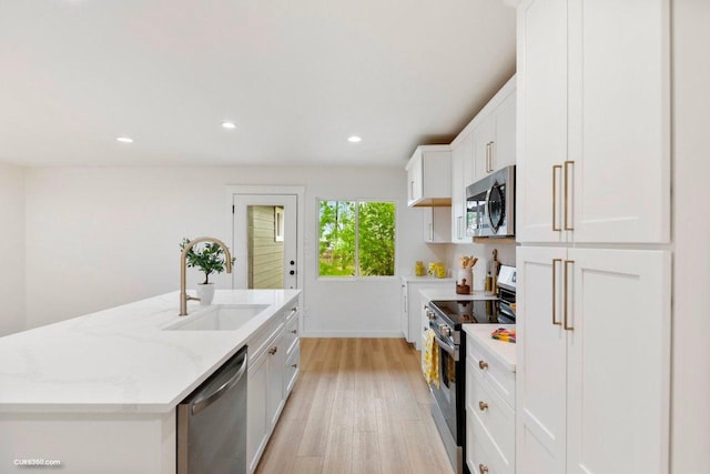 kitchen with appliances with stainless steel finishes, a sink, light stone counters, light wood finished floors, and white cabinetry