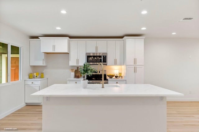 kitchen featuring light wood-type flooring, white cabinetry, light stone countertops, and stainless steel appliances