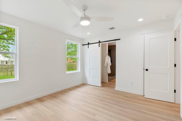 unfurnished bedroom featuring visible vents, a barn door, light wood-style flooring, and baseboards