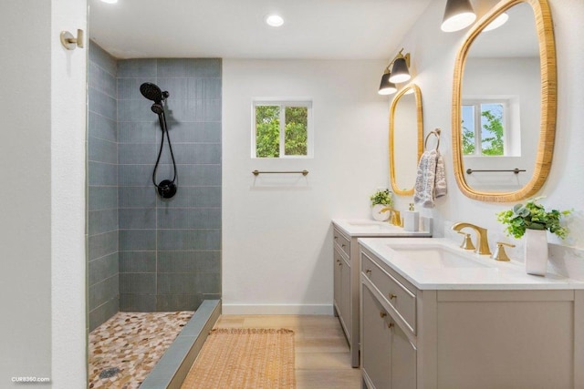 full bath with tiled shower, two vanities, a sink, and wood finished floors