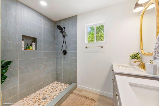 full bath with double vanity, wood finished floors, baseboards, a sink, and a tile shower