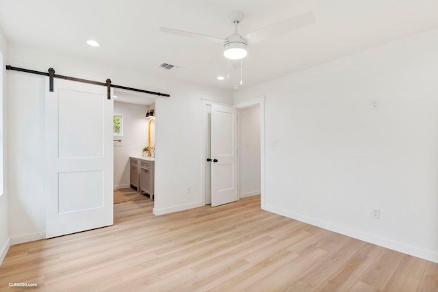 381 Perryman St, New Braunfels, TX 78130 - unfurnished bedroom featuring a barn door, light wood-type flooring, baseboards, recessed lighting, and connected bathroom