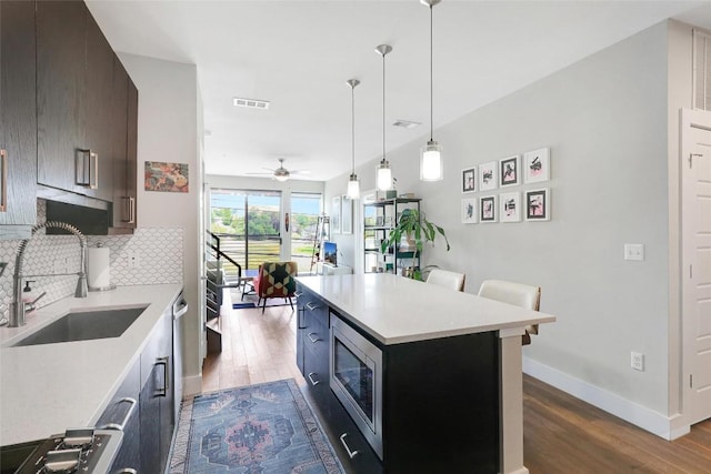 kitchen featuring visible vents, a sink, light countertops, stainless steel microwave, and dark wood-type flooring
