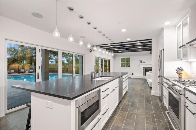 4203 Balcones Dr, Austin, TX 78731 - kitchen featuring a sink, appliances with stainless steel finishes, dark countertops, an island with sink, and white cabinets