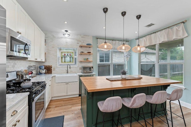 kitchen featuring visible vents, wooden counters, a center island, a sink, and stainless steel appliances