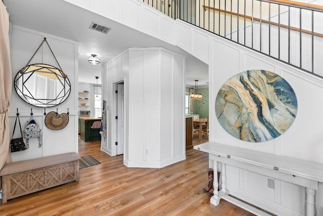 entryway featuring a towering ceiling, a notable chandelier, light wood-type flooring, and visible vents
