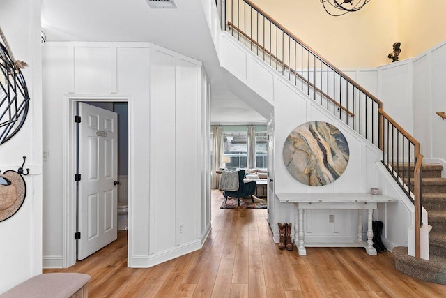 foyer entrance featuring visible vents, stairs, a towering ceiling, a decorative wall, and light wood finished floors