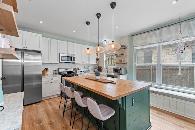 kitchen featuring light wood finished floors, wooden counters, a center island, stainless steel appliances, and white cabinetry