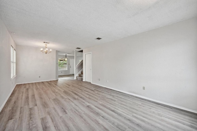 unfurnished living room featuring a textured ceiling, a notable chandelier, wood finished floors, and stairway