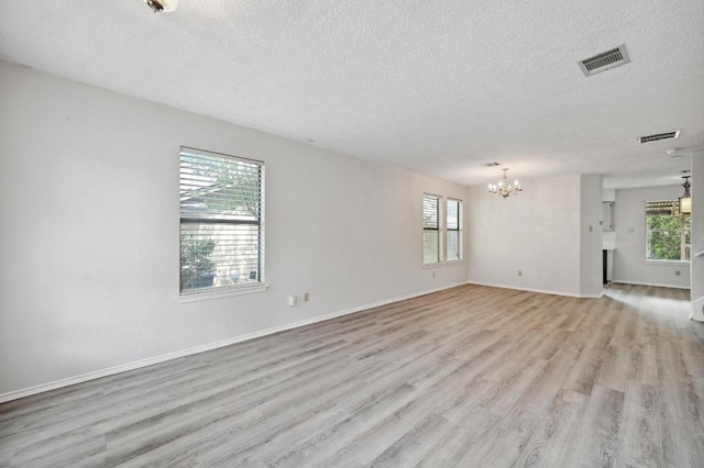 unfurnished living room with a textured ceiling, a chandelier, light wood finished floors, and visible vents