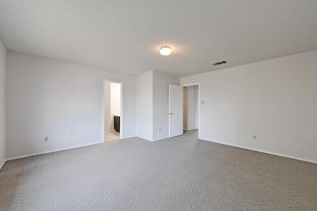 carpeted empty room featuring visible vents, a textured ceiling, and baseboards