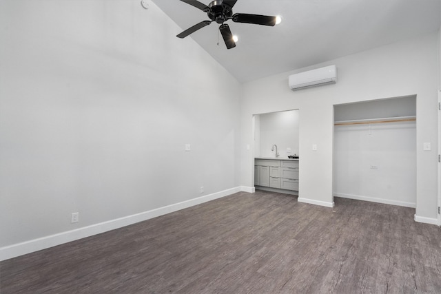 unfurnished bedroom featuring baseboards, high vaulted ceiling, a wall mounted AC, a sink, and dark wood finished floors