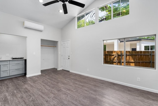 unfurnished bedroom with an AC wall unit, baseboards, wood finished floors, and high vaulted ceiling