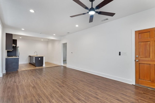 unfurnished living room with visible vents, wood finished floors, baseboards, ceiling fan, and a sink