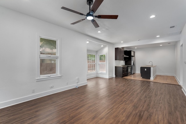 unfurnished living room with visible vents, a ceiling fan, wood finished floors, baseboards, and a sink