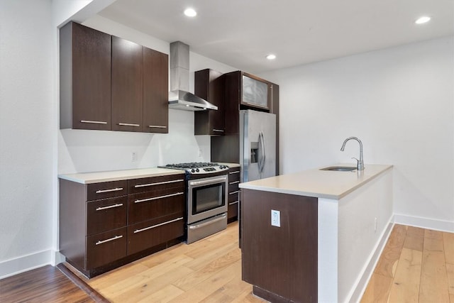 kitchen featuring a sink, appliances with stainless steel finishes, light wood-style floors, and wall chimney exhaust hood
