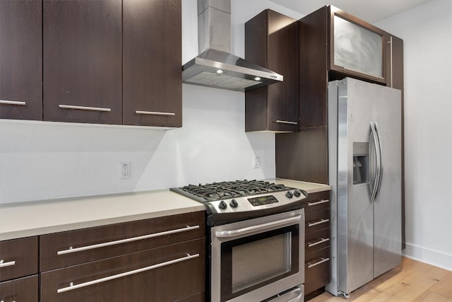 kitchen with wall chimney range hood, dark brown cabinetry, appliances with stainless steel finishes, and light wood finished floors