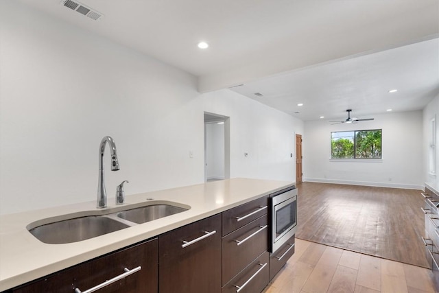 kitchen featuring visible vents, dark brown cabinets, light countertops, stainless steel microwave, and a sink
