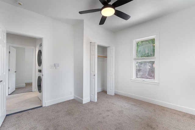 unfurnished bedroom with a ceiling fan, stacked washer / drying machine, baseboards, a closet, and carpet