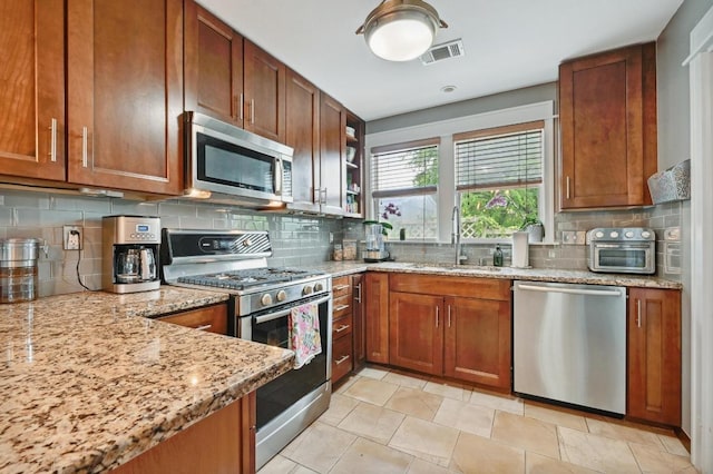 1185 Coleto St, Austin, TX 78702 - kitchen featuring appliances with stainless steel finishes, decorative backsplash, light stone countertops, and brown cabinets
