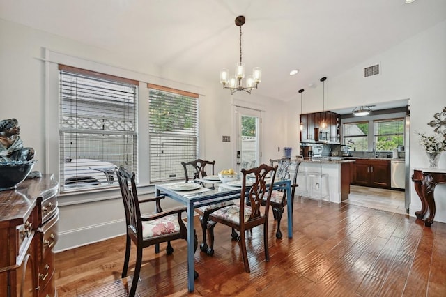 dining area with a chandelier, hardwood / wood-style floors, plenty of natural light, lofted ceiling, and baseboards