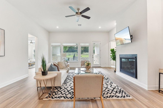 living area with baseboards, a ceiling fan, a glass covered fireplace, and wood finished floors