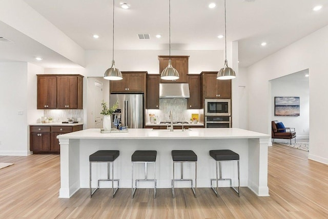 kitchen featuring visible vents, under cabinet range hood, light wood-style flooring, appliances with stainless steel finishes, and backsplash