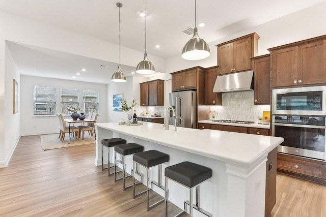 kitchen with light countertops, under cabinet range hood, light wood-style flooring, appliances with stainless steel finishes, and backsplash
