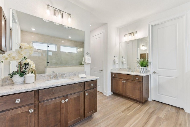 full bath featuring a sink, walk in shower, wood finished floors, and two vanities