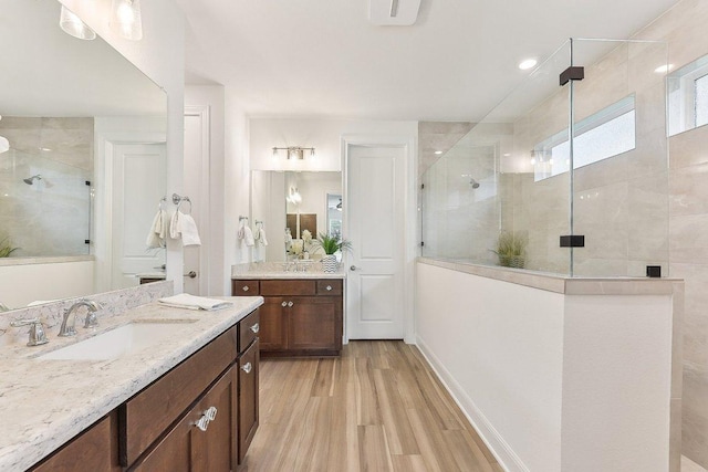 bathroom with wood finished floors, baseboards, two vanities, a shower stall, and a sink