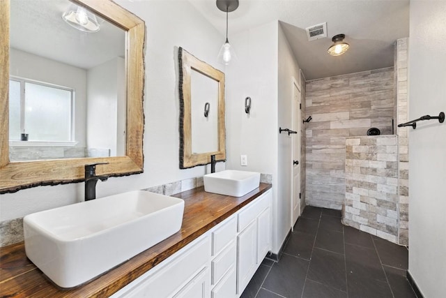 bathroom featuring tile patterned flooring, a sink, a tile shower, and double vanity