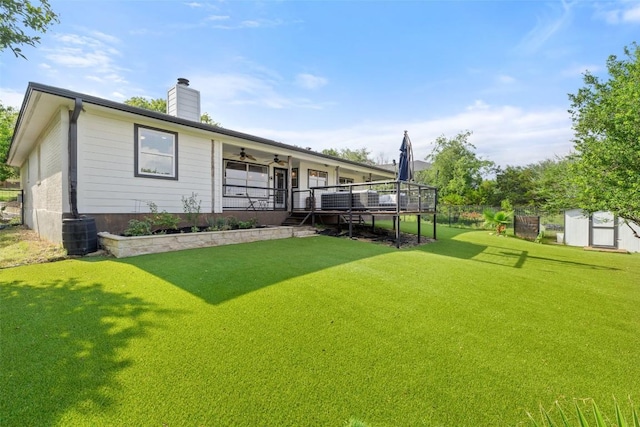 back of property featuring an outdoor structure, a chimney, a ceiling fan, a storage shed, and a yard
