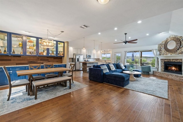 living area with a ceiling fan, visible vents, vaulted ceiling, a brick fireplace, and recessed lighting