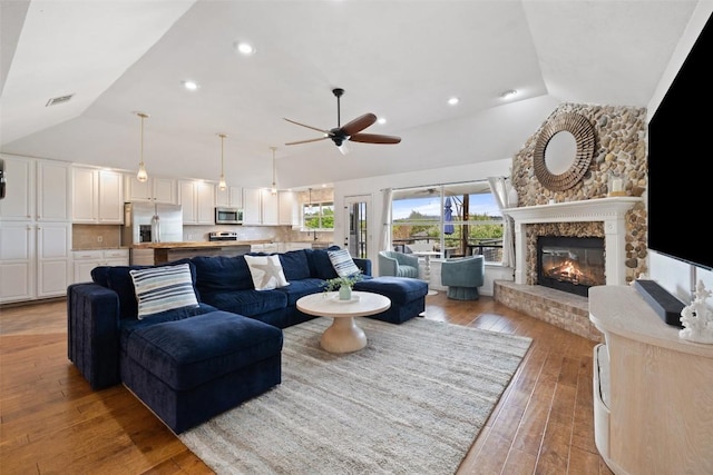 living room featuring a ceiling fan, visible vents, a large fireplace, high vaulted ceiling, and light wood-style flooring