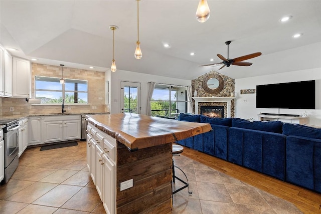 kitchen with a ceiling fan, vaulted ceiling, stainless steel electric range, open floor plan, and a glass covered fireplace