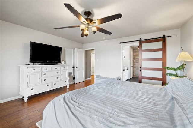 bedroom with a ceiling fan, a barn door, baseboards, ensuite bath, and dark wood-type flooring