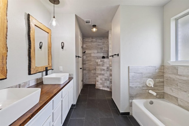 bathroom featuring tiled shower, tile patterned floors, visible vents, and a sink