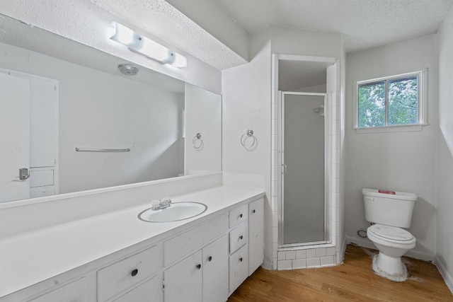 full bath featuring vanity, toilet, a textured ceiling, wood finished floors, and a stall shower