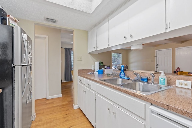 kitchen featuring freestanding refrigerator, white cabinets, a sink, and light wood-type flooring