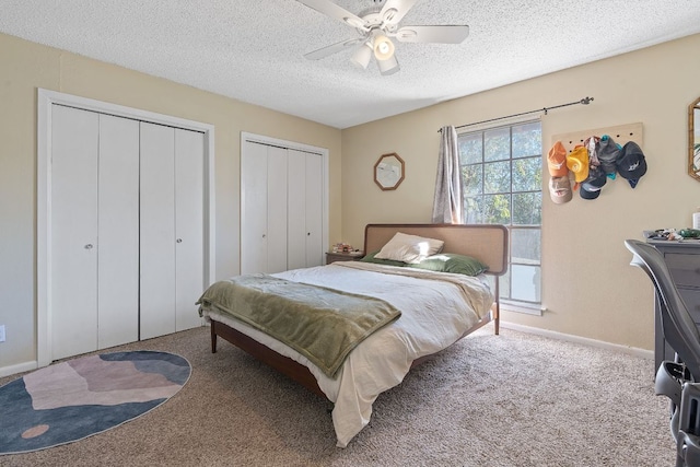bedroom with carpet floors, multiple closets, baseboards, a textured ceiling, and a ceiling fan