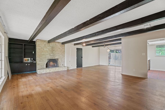 unfurnished living room featuring baseboards, wood finished floors, a fireplace, and beamed ceiling